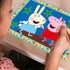 Child painting Ravensburger CreArt Jr Peppa Pig artwork with brush, showing Peppa and friend framed in colorful border with bright background.