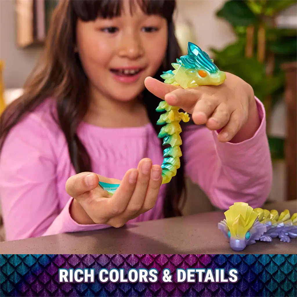 Articulated dragon toy in glossy teal and yellow plastic with crystal-textured scales and flexible joints, held in a child’s hands during play at a table, emphasizing rich colors and detailed design.