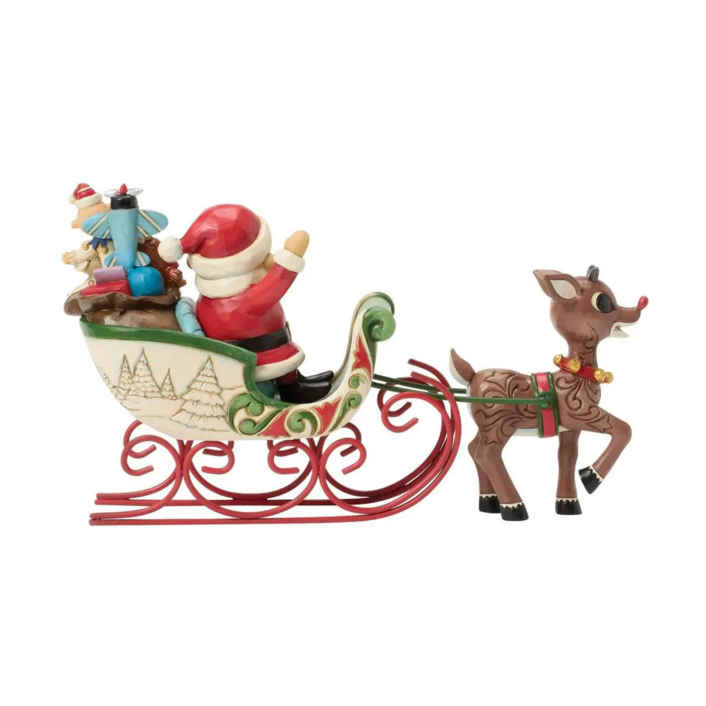 Alternate side view of Jim Shore Rudolph and Santa sleigh figurine, with visible folk art swirls on Rudolph and gifts in sleigh.