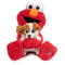 Sitting plush Elmo in fuzzy red fabric hugging small puppy Tango, smiling with wide open mouth, featuring soft textures and stitched paw detail for playtime fun.