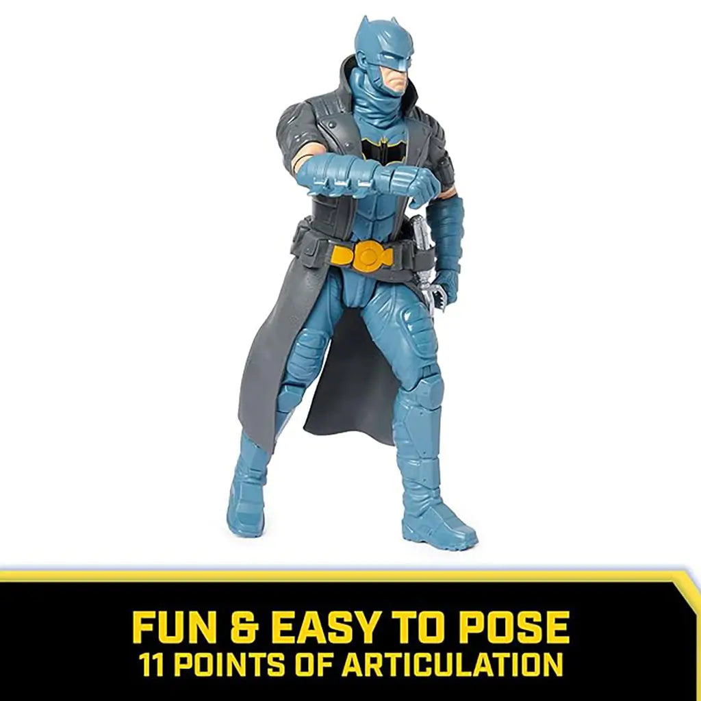 Poseable DC Comics Batman 12-inch action figure in gray and blue suit with trench coat, standing in a battle-ready stance with articulated arms and legs.