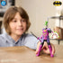 Child playing with DC Comics Ninja Strike The Joker 6-inch action figure, posed with sword and shield, dressed in purple armor with green hair in home setting.
