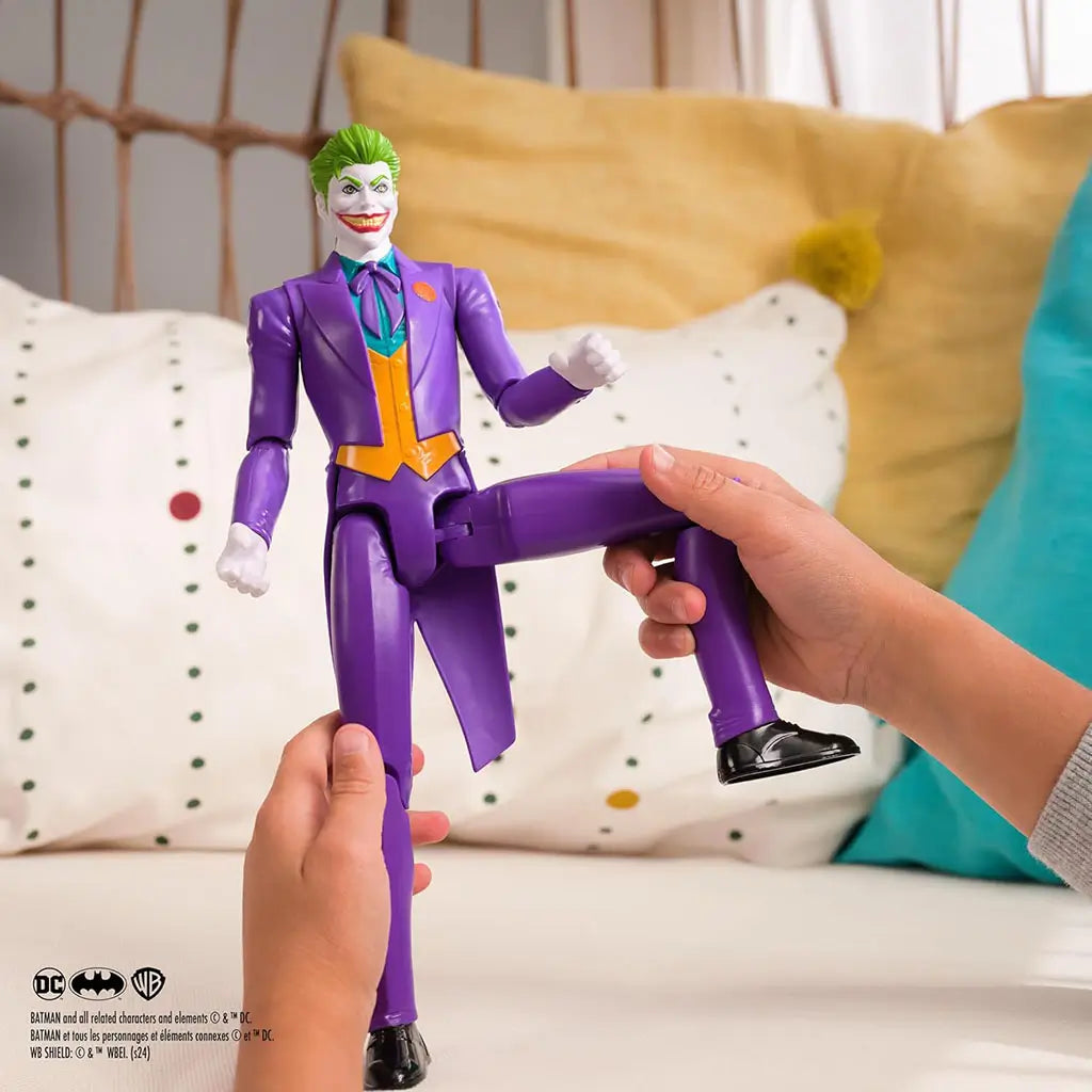 Hands holding DC Comics Joker 12-inch action figure indoors, showing articulated movement as the toy wears purple suit with green vest and iconic wide smile.