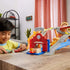 Disney Pixar Cars toy raceway playset in colorful molded plastic on a wooden table, with looping tracks and Radiator Springs details, as a young child plays with Lightning McQueen and other cars indoors.