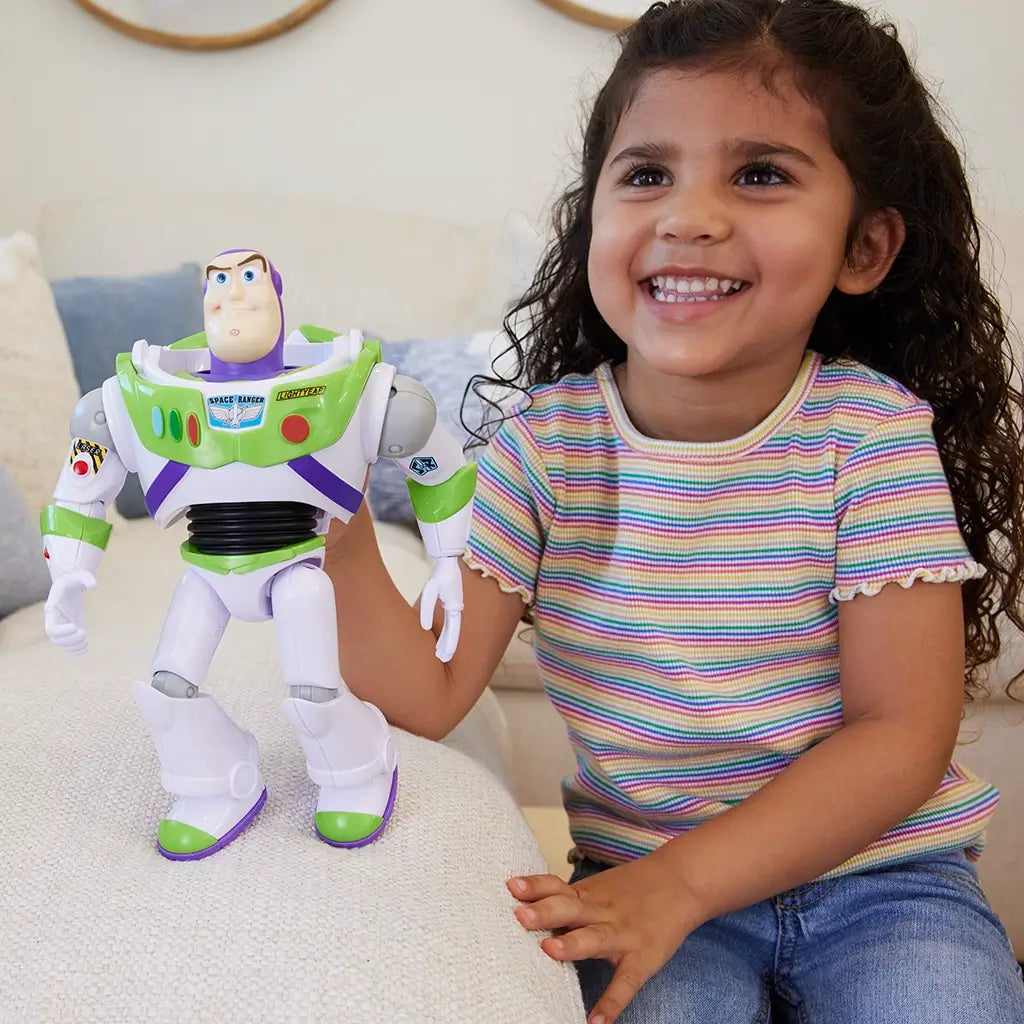 Smiling young girl in a striped shirt sitting on a couch, happily playing with a 10-inch Buzz Lightyear action figure featuring bright colors and articulated limbs.