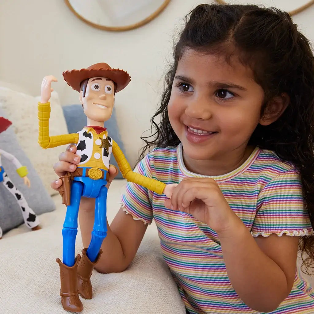 Smiling young girl holding Disney and Pixar Toy Story Woody 12-inch action figure, dressed in cowboy outfit with brown hat, sitting on a couch and engaging with the toy.