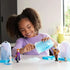 Smiling child playing with Disney Frozen Ice Reveal figures of Anna, Kristoff, and Olaf while scooping blue ice gel from a crystal-shaped container in a bright, cozy room setting.