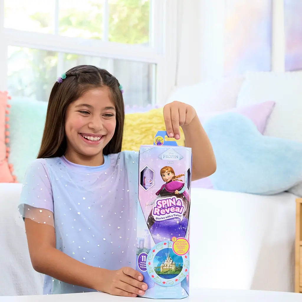Smiling child in light blue shirt holding Disney Frozen Spin & Reveal Anna doll box, featuring colorful graphics and interactive surprise compartments.