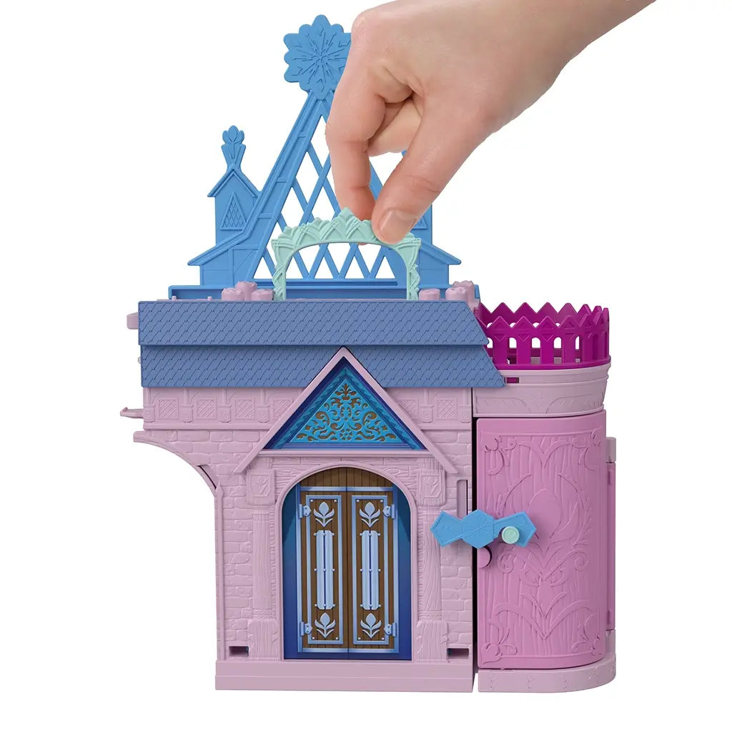 Hand carries Disney Frozen Storytime Stackers Anna’s Arendelle Castle in closed compact form, with blue rooftop, pink tower, and decorated brown double doors for storage.