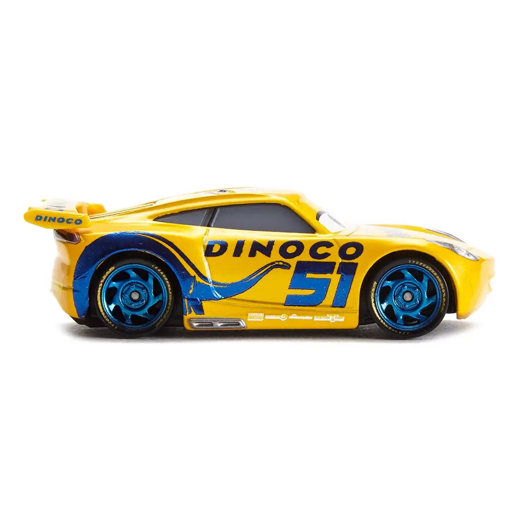 Disney Pixar Cars Dinoco Cruz Ramirez diecast left side view displaying bright yellow metal finish, smooth aerodynamic profile, flowing blue Dinoco wave graphics, large number 51, metallic blue wheels, and next-gen race car styling on white.