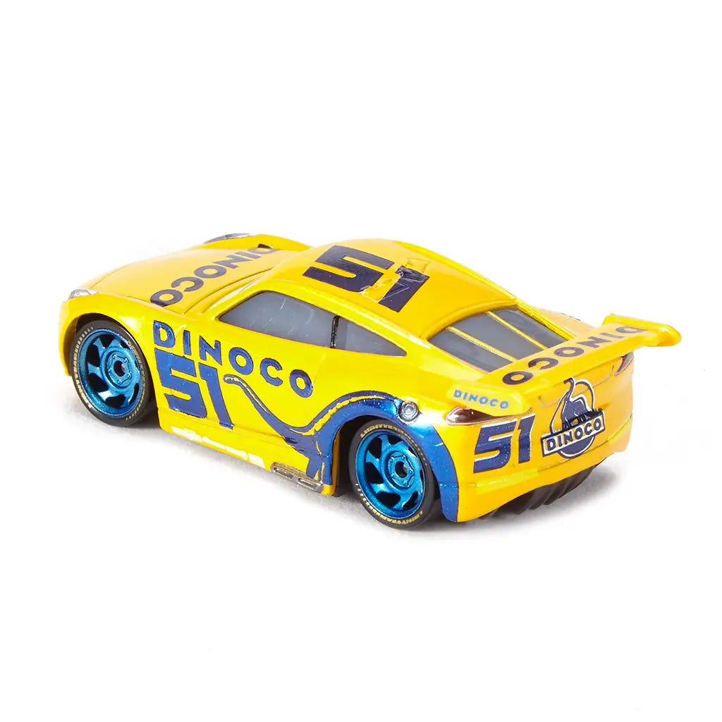 Disney Pixar Cars Dinoco Cruz Ramirez diecast shown from a rear angled view, highlighting the bright yellow metal body, blue Dinoco rear spoiler, sculpted diffuser, metallic blue wheels, and modern stock car proportions against a white background.