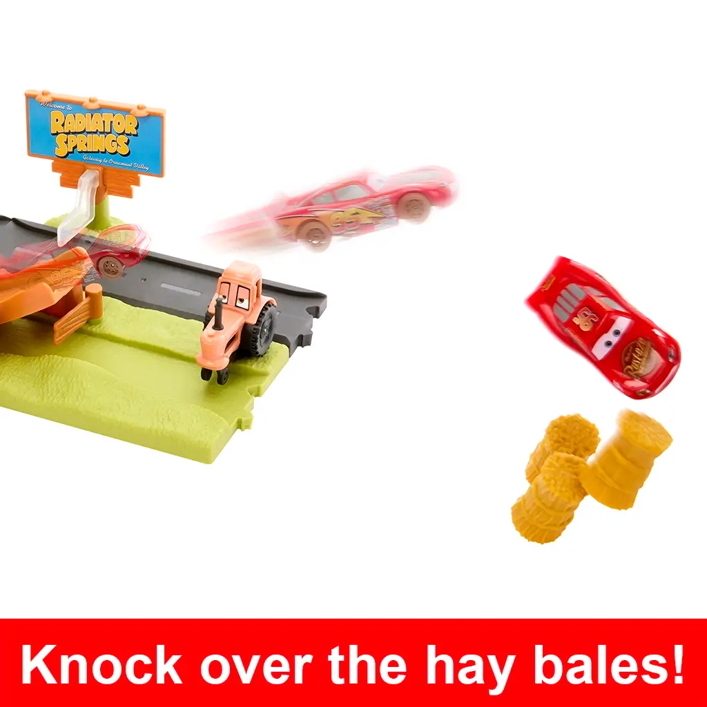 Disney Pixar Cars toy playset showing Lightning McQueen car midair after racing down track, knocking over bright yellow hay bale obstacles beside Radiator Springs sign.