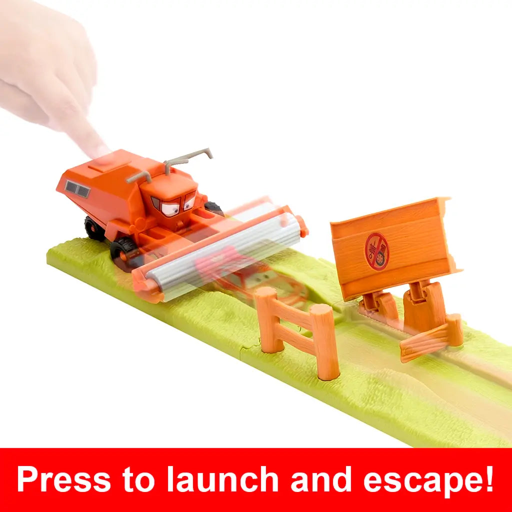 Disney Pixar Cars playset close-up with child pressing orange Frank harvester to launch Lightning McQueen down green ramp, passing wooden fences and sign obstacles.