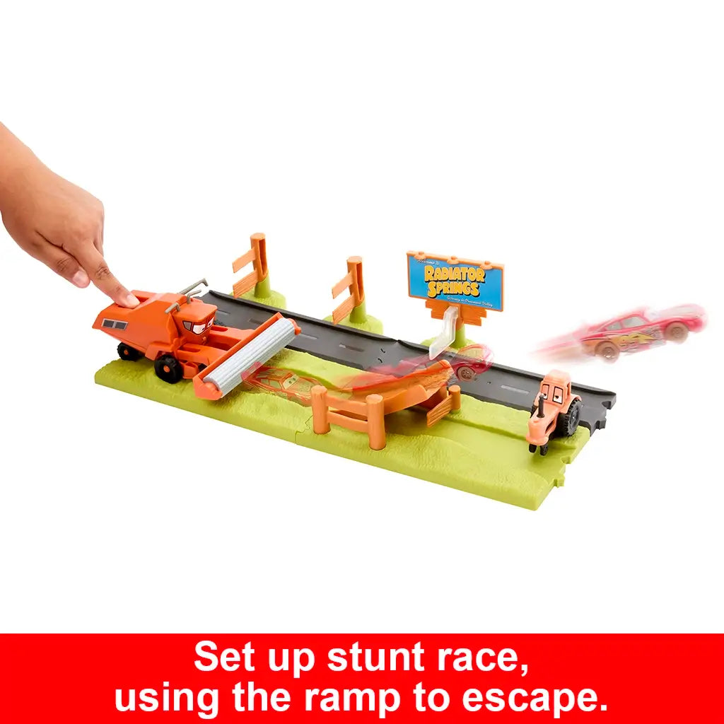 Disney Pixar Cars stunt race playset with colorful ramp, roadway, and Radiator Springs sign, featuring Lightning McQueen launched forward past orange tractor and hay bale obstacles.