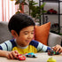 Disney Pixar Cars diecast vehicles in a lifestyle scene with a smiling child playing at a table, colorful metal character cars, rounded toy shapes, and a warm living room background.