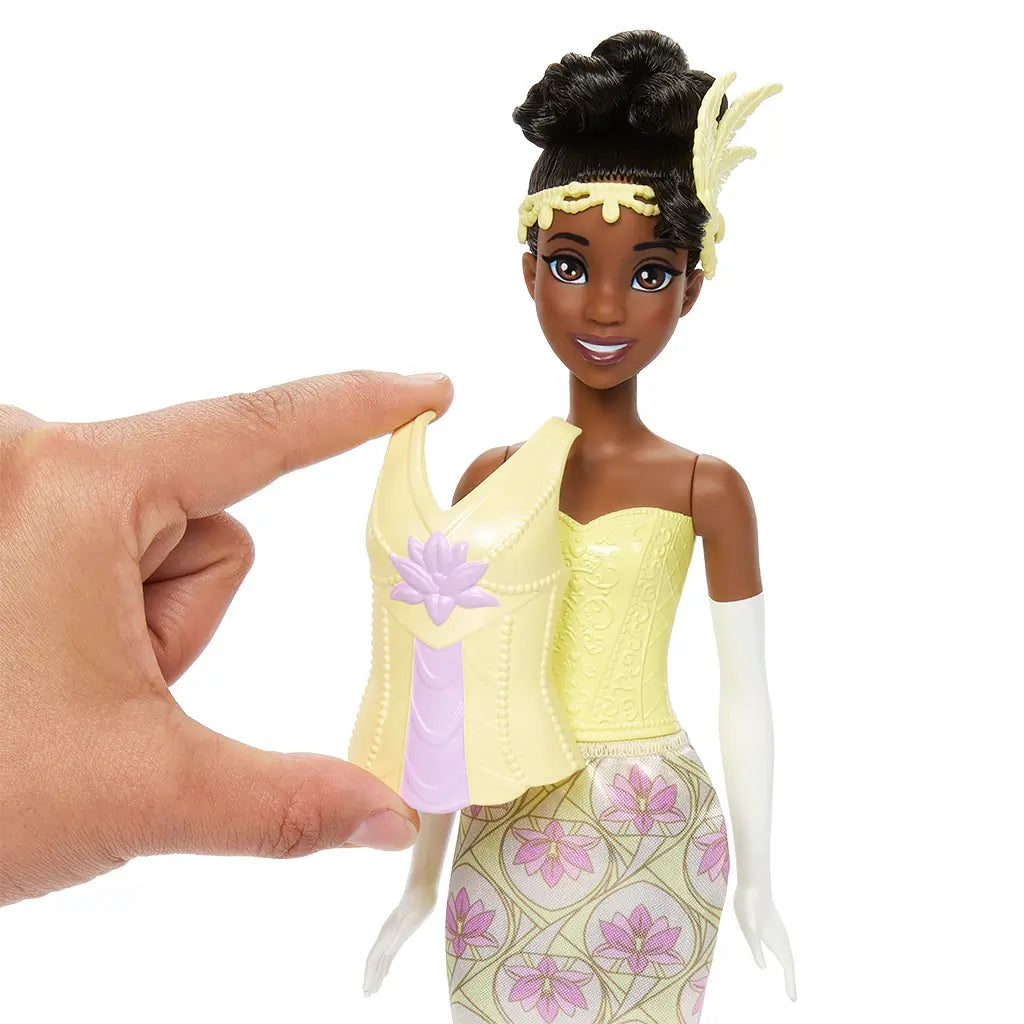 Disney Princess Tiana doll shown with hand holding removable yellow bodice, highlighting snap-on style feature for quick outfit changes between her two storytelling looks.
