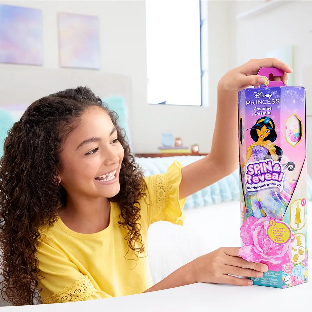 Smiling girl in yellow shirt holding Disney Princess Spin & Reveal Jasmine doll packaging, ready to open for surprise accessories and play.