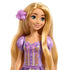 Close-up of Rapunzel doll’s smiling face with green eyes, freckles, and a lavender flower hair clip, wearing a purple and pink floral dress with gold decorative details.