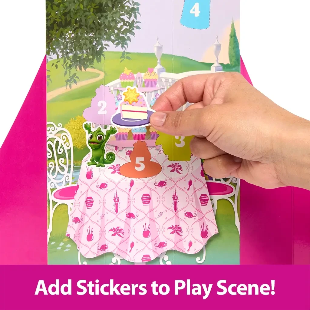 Hand placing a cake sticker on a colorful interactive play scene featuring numbered pop-out doors, cupcakes, Pascal the chameleon, and a pink tablecloth with icons.