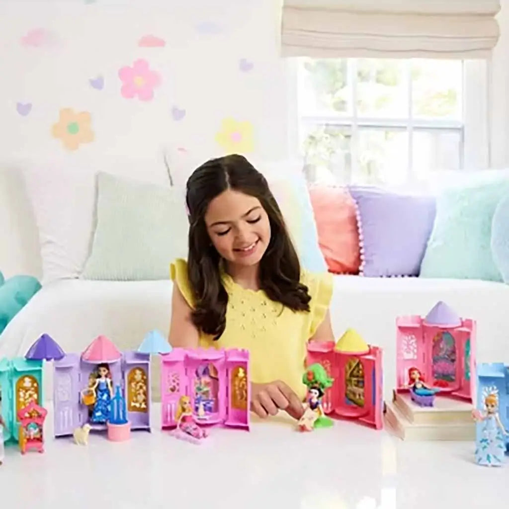 Smiling child in a yellow top playing with multiple Disney Princess Tower Surprise playsets, each castle featuring miniature princess figures like Belle, Snow White, and Ariel on a white play table.