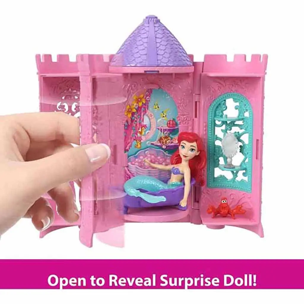 Disney Princess Tower Surprise playset being opened by hand to reveal Ariel figure inside, displaying purple and teal castle interior and text reading “Open to Reveal Surprise Doll!” on bottom banner.