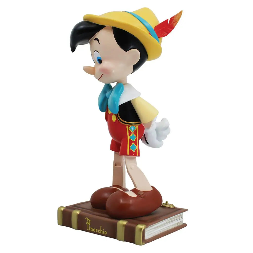 Side view of Pinocchio 9-inch figurine wearing feathered hat and colorful outfit, standing on detailed book base; Disney Showcase Pinocchio 85th collectible.