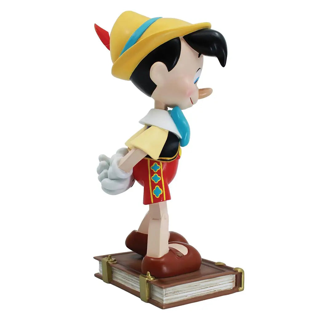 Profile view of Pinocchio 9-inch figurine featuring wooden limbs, red feathered hat, and book base with gold accents; part of Disney Showcase 85th anniversary series.
