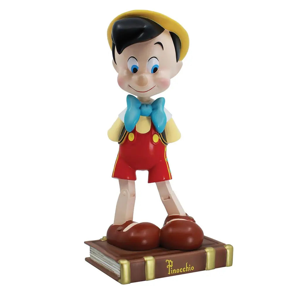 Front view of 9-inch Pinocchio figurine standing on a book base, dressed in red shorts, blue bow, and yellow hat; part of Disney Showcase 85th anniversary collection.