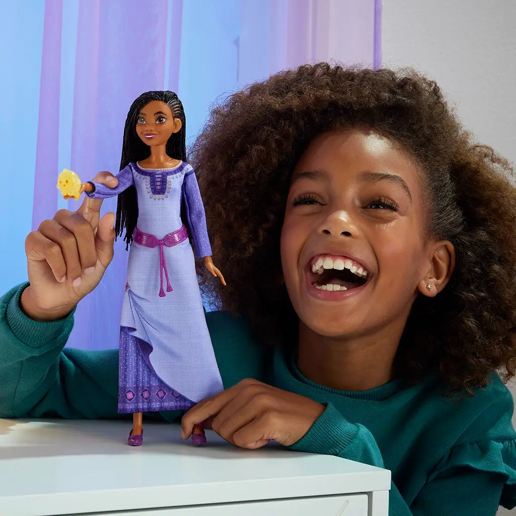 Smiling child playing with Disney Wish Singing Asha of Rosas doll, holding the toy with attached Star character in a brightly lit room, showcasing interactive play.