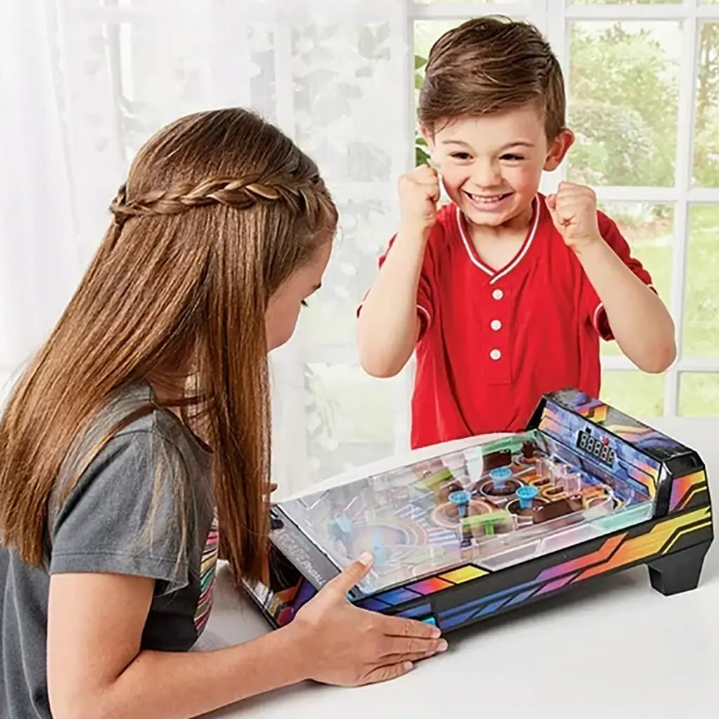 Young boy in red shirt cheers excitedly while a girl plays with the colorful Epoch Game Zone electronic arcade pinball machine on a white table by the window.