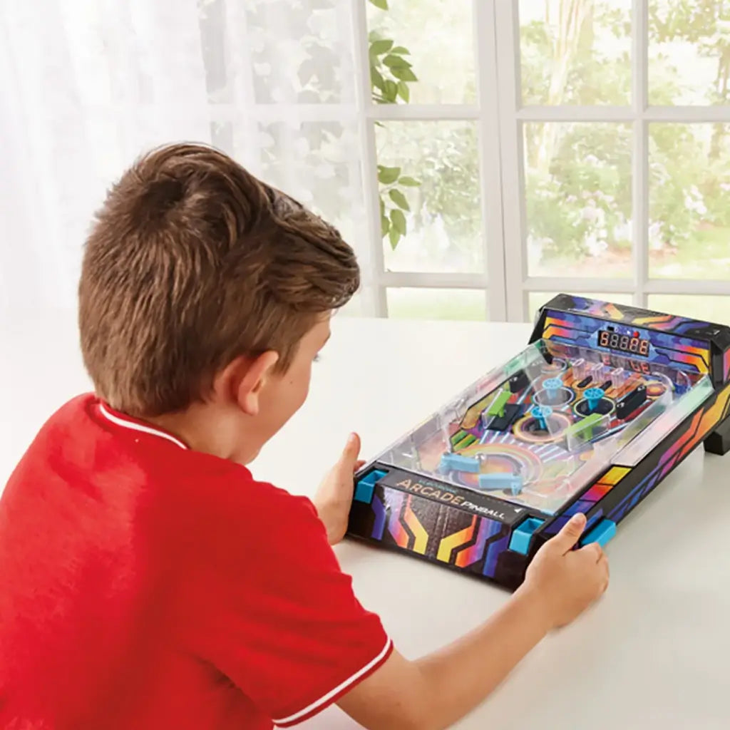 Boy in a red shirt sits at a table playing Epoch Game Zone electronic arcade pinball, focusing on flippers and scoring on the bright neon playfield.