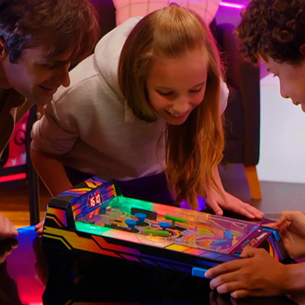 Group of smiling children gathered around Epoch Game Zone electronic pinball machine in a dimly lit room, watching LED lights glow as the game is played.