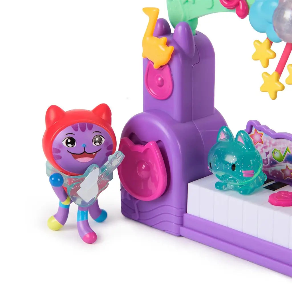 Gabby's Dollhouse Paw-some Party Story playset close-up in bright purple plastic showing smiling cat character holding translucent guitar beside cat-ear speaker and keyboard stage