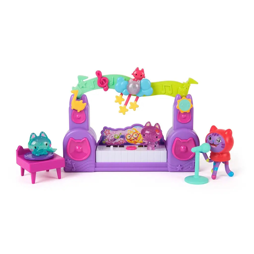 Gabby's Dollhouse The Movie Paw-some Party Story playset in purple and pink plastic with cat-shaped speakers, rainbow music arch, keyboard stage, and mini cat figures arranged on a white background.
