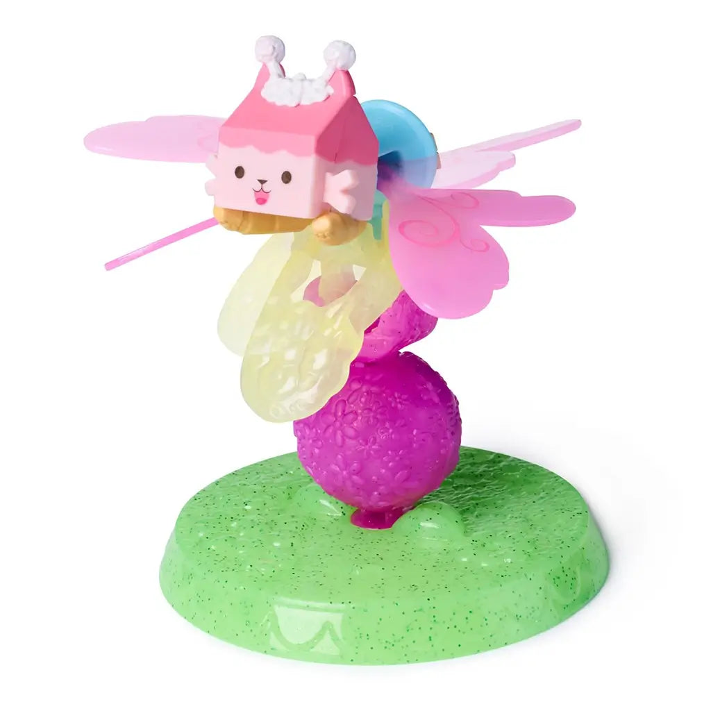Gabby’s Dollhouse Baby Box Cat fairy figure in pink, yellow, and green glossy plastic with winged shape and textured base stand, designed for imaginative play, displayed on a white background.