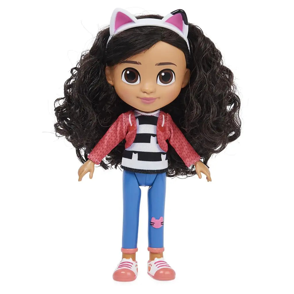 Gabby's Dollhouse Gabby Girl doll in pink jacket and blue jeans, smooth plastic fashion figure with oversized brown eyes and thick curly hair, standing upright against a clean white backdrop.