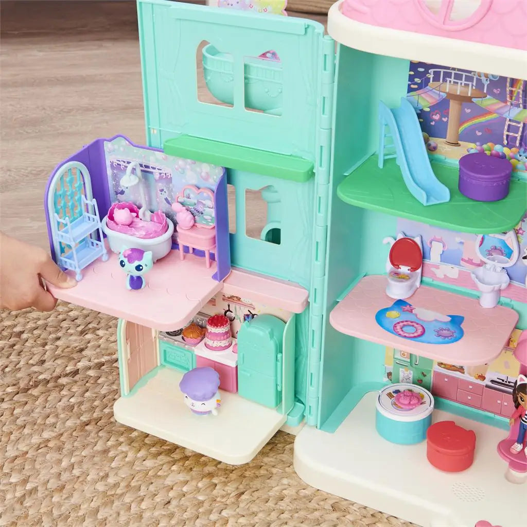 Gabby’s Dollhouse modular playset in pastel pink, teal, and purple plastic with multiple rooms and accessories, designed to connect with dollhouse sets, displayed on a woven rug background.