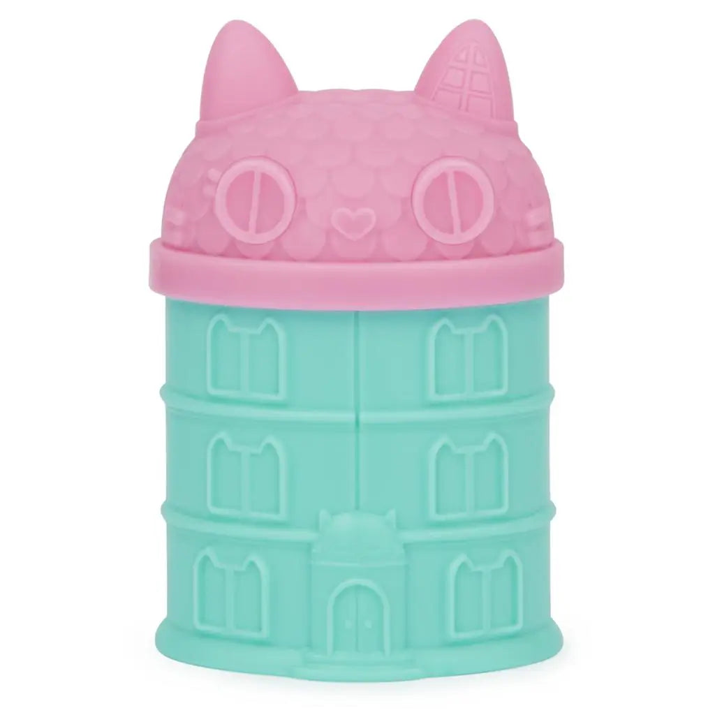 Pink and teal Gabby’s Dollhouse surprise capsule shaped like a cat-topped building with sculpted windows and doors, designed to hold mystery mini figures from the collectible toy series.