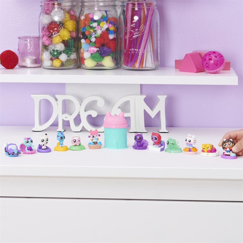 Collection of Gabby’s Dollhouse mini figures neatly lined up on a white dresser under decorative jars and a “DREAM” sign, with a teal and pink capsule displayed at the center.