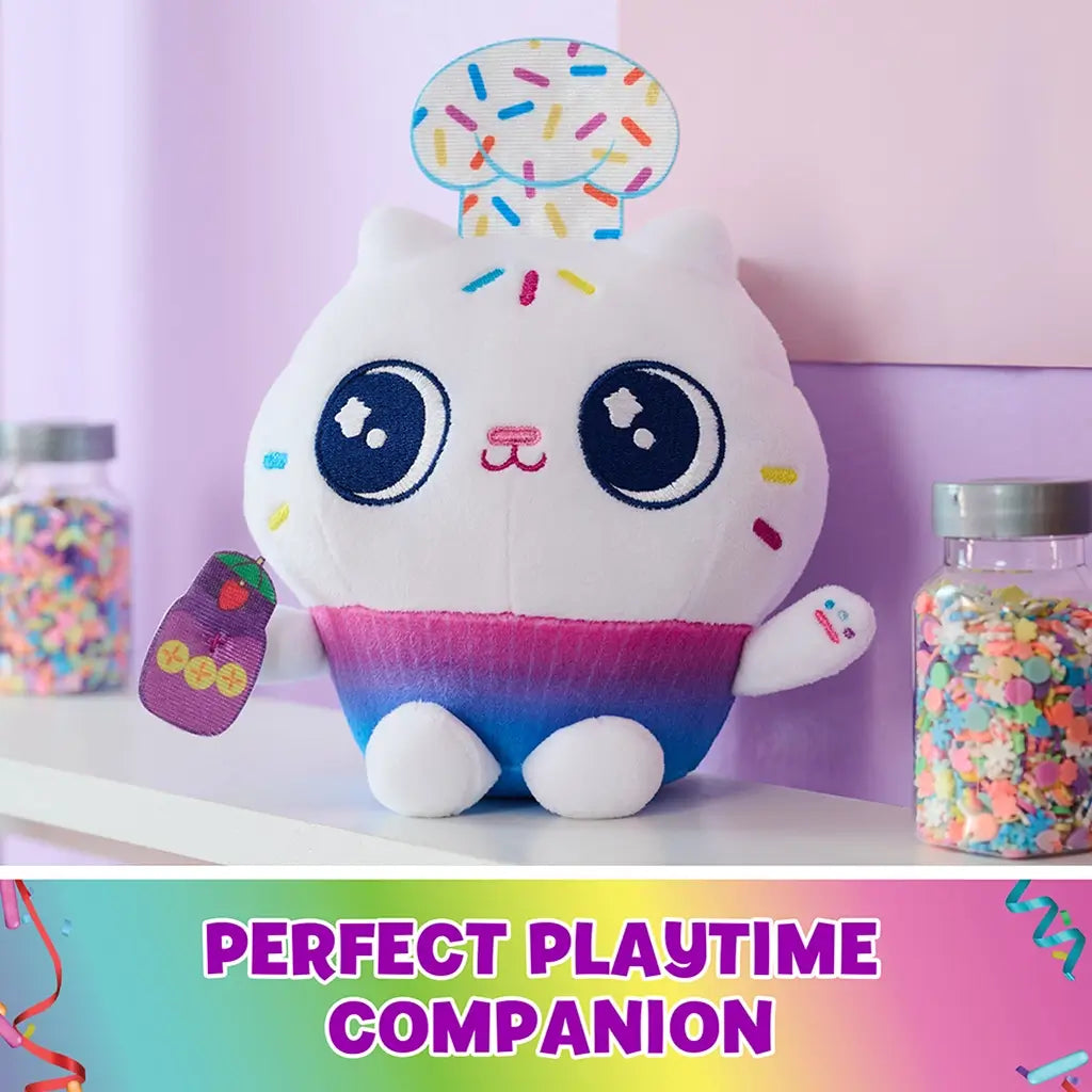 Gabby’s Dollhouse Cakey Cat plush toy white soft fabric cupcake shaped cat with rainbow gradient base, embroidered eyes and sprinkle details, playful character displayed on pastel shelf setting.