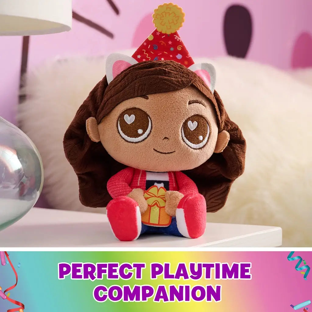 Gabby's Dollhouse plush toy in pink, red, and blue soft fabric, rounded doll form with stitched facial details and party hat, displayed on a bedside table, emphasizing imaginative playtime companion use.