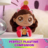 Gabby's Dollhouse plush toy in pink, red, and blue soft fabric, rounded doll form with stitched facial details and party hat, displayed on a bedside table, emphasizing imaginative playtime companion use.