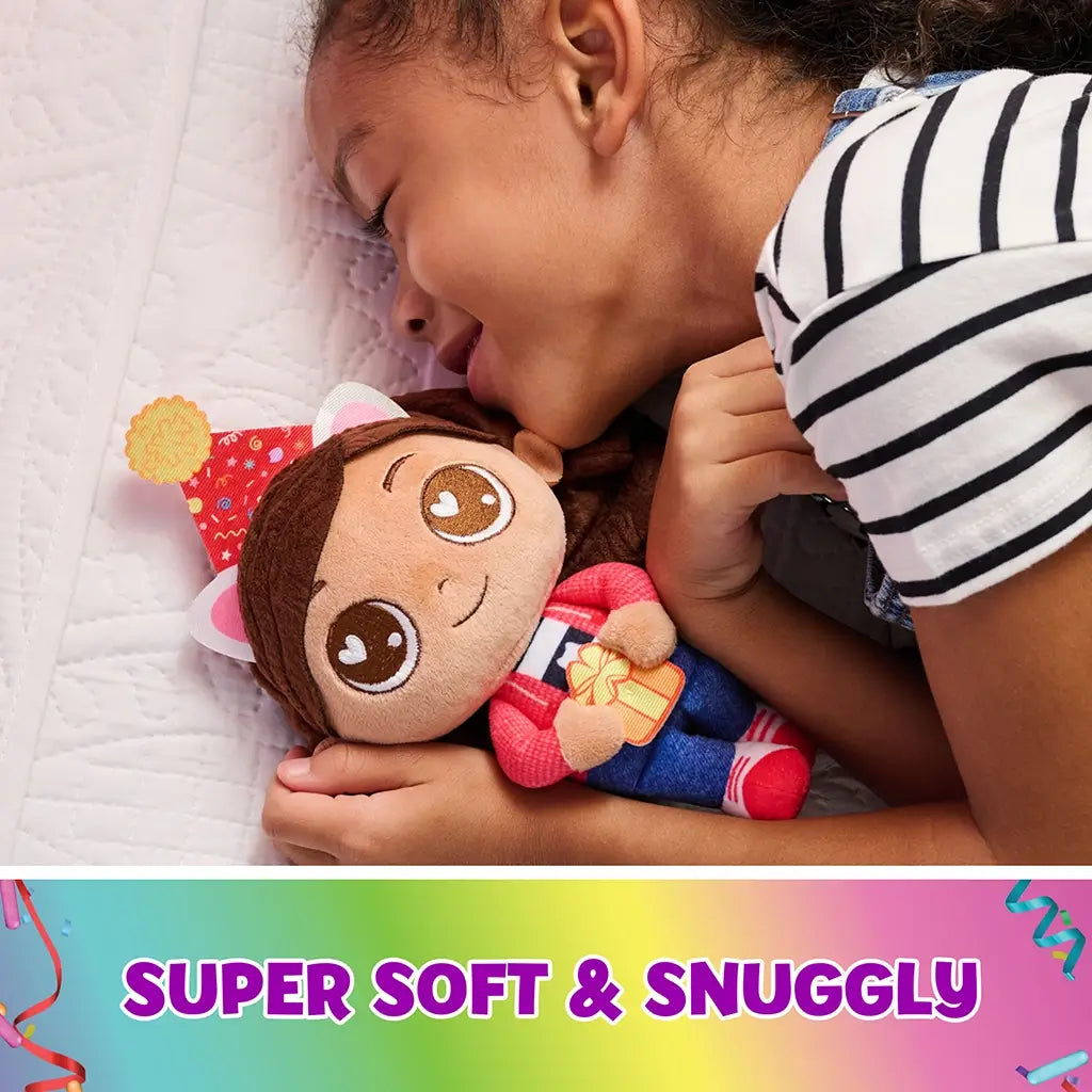 Gabby's Dollhouse plush toy in soft pastel fabric, rounded doll shape with embroidered eyes and brown yarn hair, cuddled by a child on a bed, highlighting cozy comfort and snuggly bedtime play.