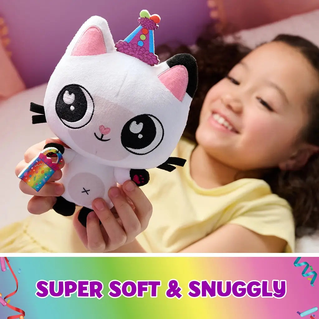 Gabby’s Dollhouse Pandy Paws plush toy white soft fabric cat with black ears, pink inner ears and embroidered face, holding rainbow accessory, cuddly character shown with child in cozy bedroom.
