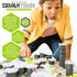 Boy in a yellow shirt leans excitedly over a GraviTrax marble run, guiding pieces as green and white tracks connect with tall grey towers on a hexagonal grid base.