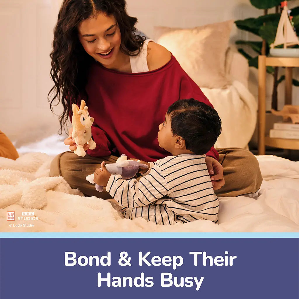 GUND Bluey plush ring rattle is shown during interactive play, featuring light blue and lavender plush fabric, a soft circular grip opening, and stitched details that keep small hands engaged.