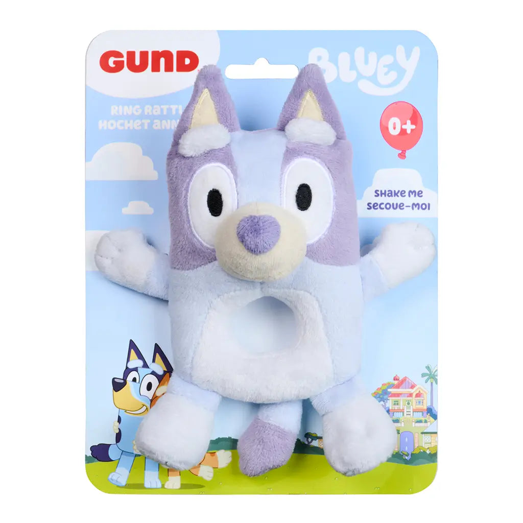 Bluey plush ring rattle displays pastel blue and lavender plush textures with embroidered eyes and smile, packaged on a branded card backing to show infant-safe design and rattle feature.
