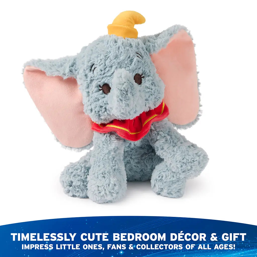 Disney Dumbo plush toy in pastel blue with gently tousled plush texture, floppy seated pose, pink ears, yellow hat, and red collar, styled as timeless bedroom décor and a giftable keepsake in a softly lit home environment.