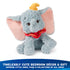 Disney Dumbo plush toy in pastel blue with gently tousled plush texture, floppy seated pose, pink ears, yellow hat, and red collar, styled as timeless bedroom décor and a giftable keepsake in a softly lit home environment.