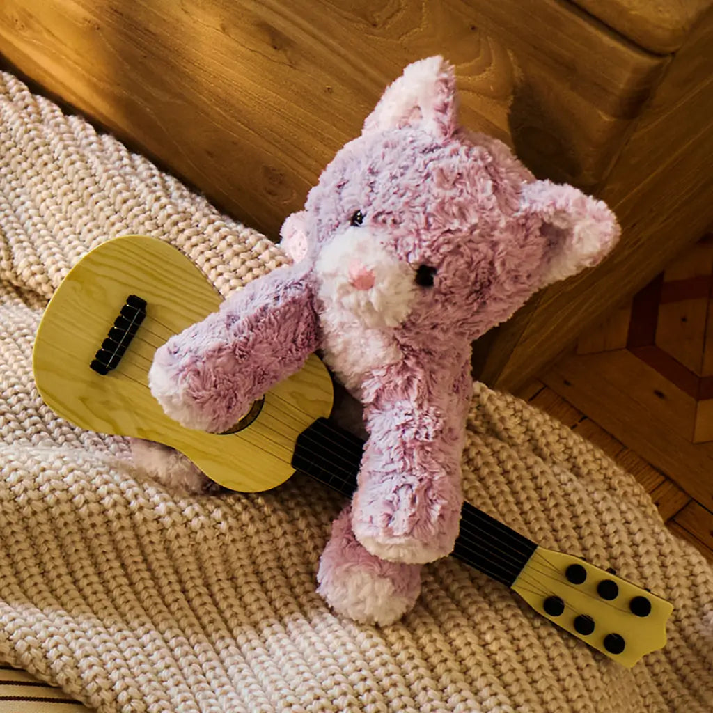 GUND Cozys Kitten plush kitten in lavender fuzzy fabric with a soft rounded body, posed holding a small toy guitar on a woven rug to suggest imaginative play, creativity, and playful nursery storytelling scenes.
